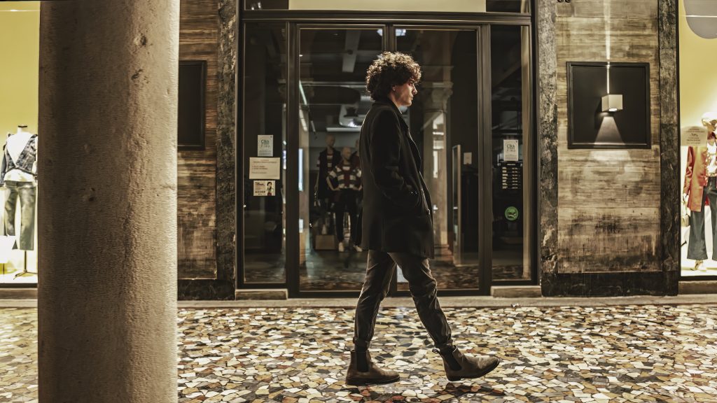 Ferrara, italy 11 april 2023: A lone young man walks through the city streets at night, illuminated by the glow of the streetlights. Moody and atmospheric.