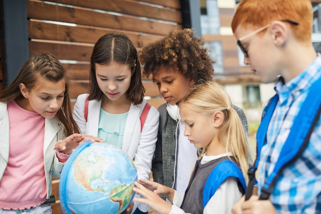 Group of multiethnic school children pointing at globe they learning the geography of their country