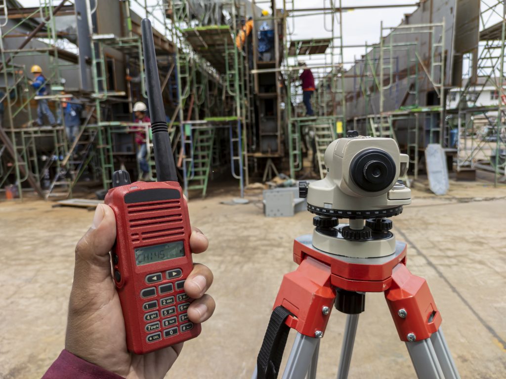 Hand holding a red radio communication and autometic levels or theodolite equipment to measuring level of steel structure at industrial factory.