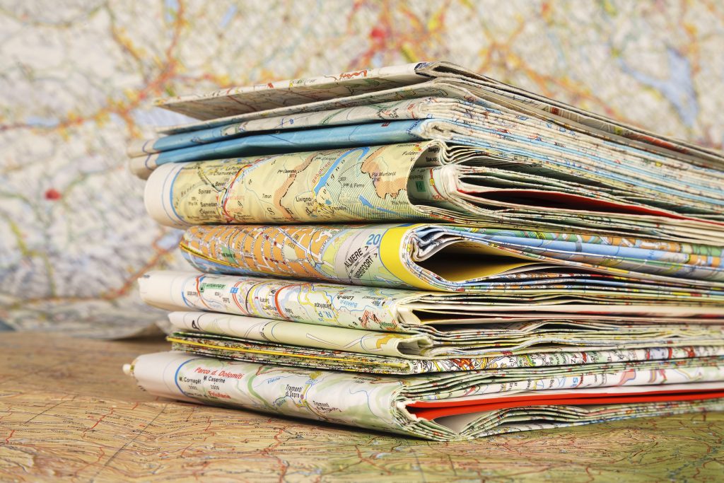 Stack of various travel maps on a open map background